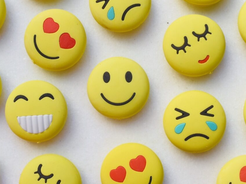 Yellow smiley face buttons display various emoji expressions, including hearts, smiles, laughter, sadness, and crying, arranged on a light background.