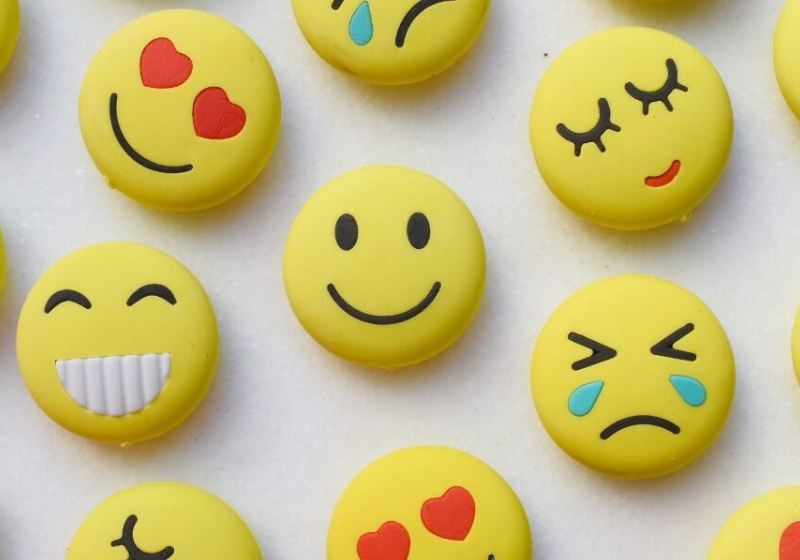 Yellow smiley face buttons display various emoji expressions, including hearts, smiles, laughter, sadness, and crying, arranged on a light background.