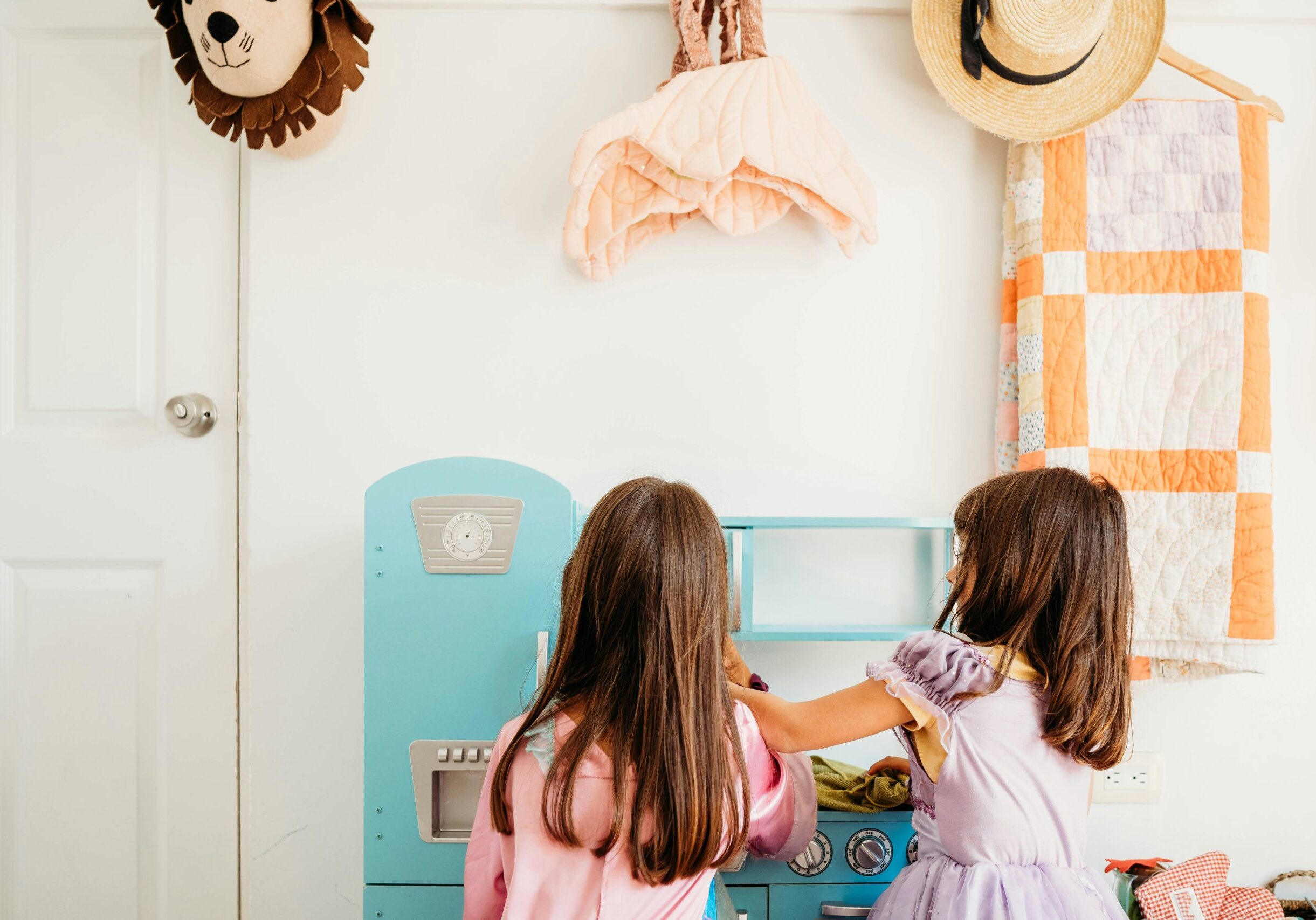 2 young girls facing away from the camera, playing at a toy kitchen